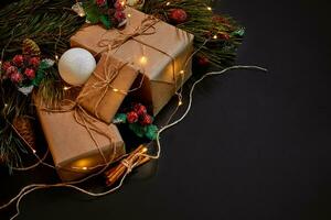 Christmas gifts and garland near green spruce branch on a black background. Christmas background. Top view. photo