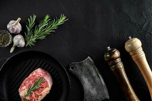 Fresh raw meat. A piece of beef tenderloin on grill pan, with a cutting ax, with spices for cooking on black stone table. Copy space photo