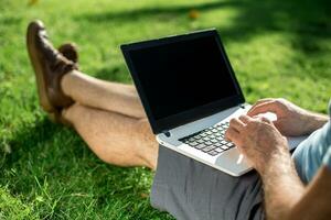 Cropped shot of man using laptop with blank screen while sitting on green grass photo