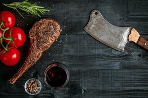 Barbecue dry aged rib of beef with spice, vegetables and glass of red wine close-up on black wooden background photo