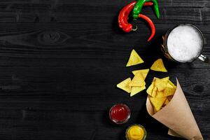 Snack for party, chips, nachos with sauces tomato ketchup , mustard and mug of beer on a black background. Top view, copy space photo