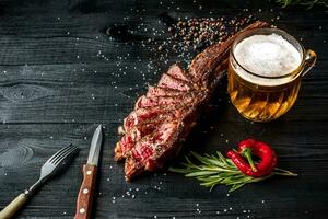 Barbecue dry aged rib of beef with spice, vegetables and a glass of light beer close-up on black wooden background photo