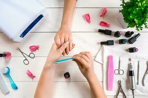 Manicure for the client. Close-up of the hands of a manicurist and client on a wooden background photo