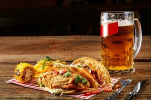 First corn tortilla with grilled chicken fillet, second with fish fillet, sauce and beer on wooden table photo