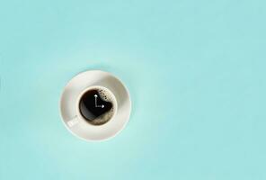 Arrows of a clock in a cup of coffee on blue background. View from above. photo