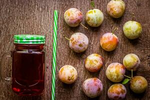 Glass with fresh Plum Juice on vintage wooden background photo