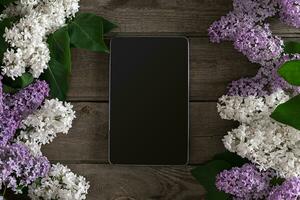 Lilac blossom on rustic wooden background, tablet with empty space for greeting message. Top view photo