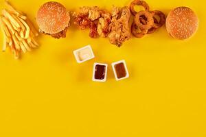 Fast food dish top view. Meat burger, potato chips and wedges. Take away composition. French fries, hamburger, mayonnaise and ketchup sauces on yellow background. photo