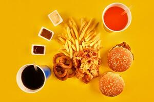 Fast food concept with greasy fried restaurant take out as onion rings, burger, fried chicken and french fries as a symbol of diet temptation resulting in unhealthy nutrition. photo