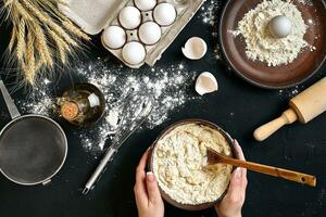 Female hands making mixing dough in brown bowl on black table, baking preparation close-up. photo