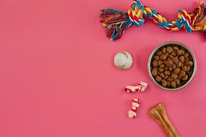 Toys -multi coloured rope, ball, dry food and bone. Accessories for play on pink background top view photo