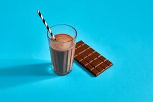 Glass of chocolate milk with chocolate bar on blue background with space for text or design photo