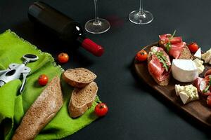 Wine bottle with cheese and traditional sausages on wooden board on black background with copy space photo