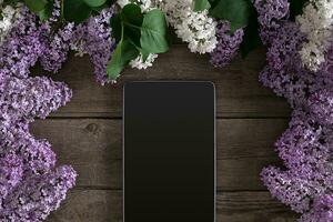 Lilac blossom on rustic wooden background, tablet with empty space for greeting message. Top view photo