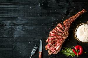 Barbecue dry aged rib of beef with spice, vegetables and a glass of light beer close-up on black wooden background photo