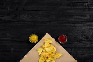 Tortilla chips with mustard and tomato sauce on black wooden table. Top view photo