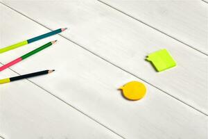 Colorful double-sided pencils, orange and yellow sticky notes on white wooden desktop or background. Close up, copy space, top view photo