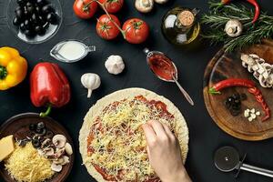 Hands of baker adding ingredients into pizza during pizza preparation at kitchen photo