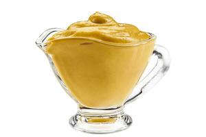 Mustard sauce in a glass sauceboat isolated on white background with copy space for text or images. Spices and herbs. Close-up shot. photo