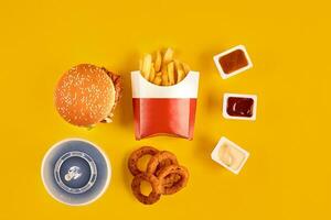 Fast food dish top view. Meat burger, potato chips and wedges. Take away composition. French fries, hamburger, mayonnaise and ketchup sauces on yellow background. photo