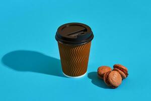 Hot coffee in brown paper cup with black lid and macaroons on bl photo