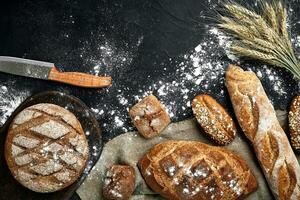 parte superior ver de junquillo, horneado pan, harina y trigo Picos composición con trigo harina rociado alrededor en un oscuro antecedentes foto