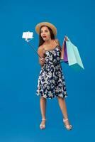 Young woman in casual clothes with shopping bags using selfie stick to take a self portrait on blue studio background with copy space photo