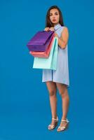 Photo of beautiful young woman with colorful shopping bags on the wonderful blue background