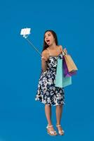 Young stylish woman posing and taking a selfie on the phone with shopping bags on a blue background photo