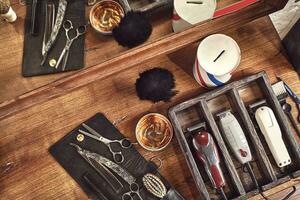 Hairdresser tools on wooden background. Top view on wooden table with scissors, comb, hairbrushes and hairclips, trimmer. photo