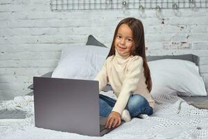 Cute little girl girl feeling amusing while watching cartoons on a laptop sitting on bed photo