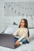 Cute little girl girl feeling amusing while watching cartoons on a laptop sitting on bed photo