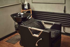 negro cuero asiento con lavar cuenca en un barbería interior con toallas y champú en el lado. foto