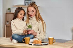 Nice smiling mother giving croissant to her child sitting on the kitchen photo