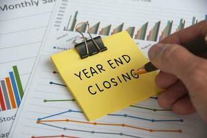 Hand writing Year End Closing text on sticky note with statistic and graph background photo