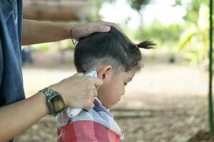 Barbero corte pelo de un asiático chico en un abierto espacio lleno con arboles foto