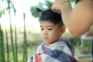 Barbero corte pelo de un asiático chico en un abierto espacio lleno con arboles foto