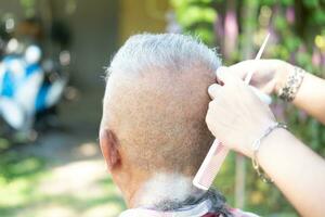un mayor asiático persona obtiene su pelo cortar al aire libre. foto