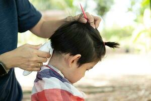 Barbero corte pelo de un asiático chico en un abierto espacio lleno con arboles foto