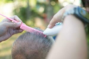 An elderly Asian person gets his hair cut outdoors. photo