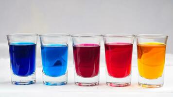 Small glasses filled with colorful water are neatly arranged on an isolated white background photo