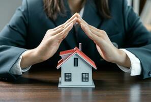 Concept of home and real estate Property insurance, insurance protective hand over house for protection and care, Home protection concept, close up of female hands sheltering modern house. photo