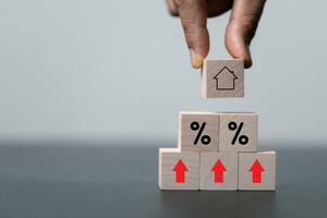 House and property investment and asset management concept. Interest rates, loan mortgage, house tax. Hand holding house icon on wooden block from stack with percent icon. Copy space for text. photo