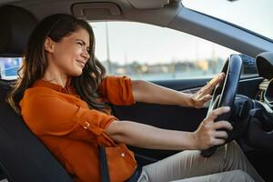 contento mujer conducción un coche y sonriente. linda joven éxito contento morena mujer es conducción un coche. retrato de contento hembra conductor direccion coche con la seguridad cinturón foto