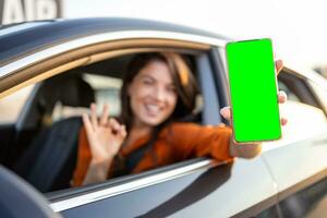 Female driver using digital app in mobile phone. Leaning out of the car window. Chroma key on device screen photo