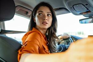 Young woman sitting on a driver's seat in the car and looking at camera over the shoulder. Portrait of pleasant female with positive expression, being satisfied with unforgettable journey by car. photo