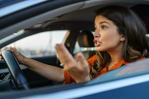 de cerca retrato, enojado joven sentado mujer Molesto apagado por conductores en frente de su. joven mujer sentado en un coche atascado en un tráfico mermelada sensación estresado porque ella es corriendo a trabajar. foto