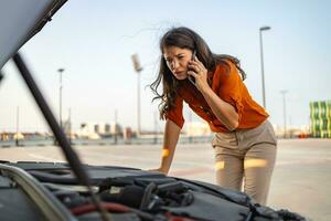 Woman with smartphone calling auto service because of car problem. Accident and breakdowns with auto concept. woman calling a car assistance service with her smartphone, her car has broken down photo