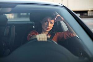 Nervous female driver sits at wheel, has worried expression as afraid to drive car by herself for first time. Frightened woman has car accident on road. People, driving, problems with transport photo