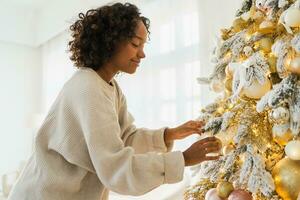 Merry Christmas. African American woman decorating Christmas tree. Happy girl near classical Christmas tree with white golden silver decorations ornament. Christmas eve at home time for celebration. photo
